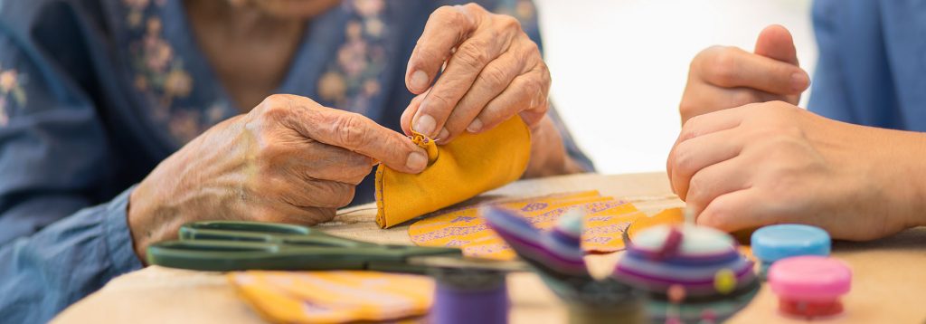 Elderly woman with caregiver in the needle crafts occupational therapy