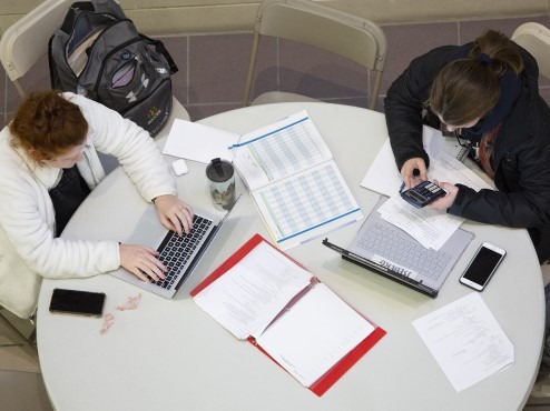 An overhead photo of two Carlow students studying on laptops at a round table surrounded by open books and binders.